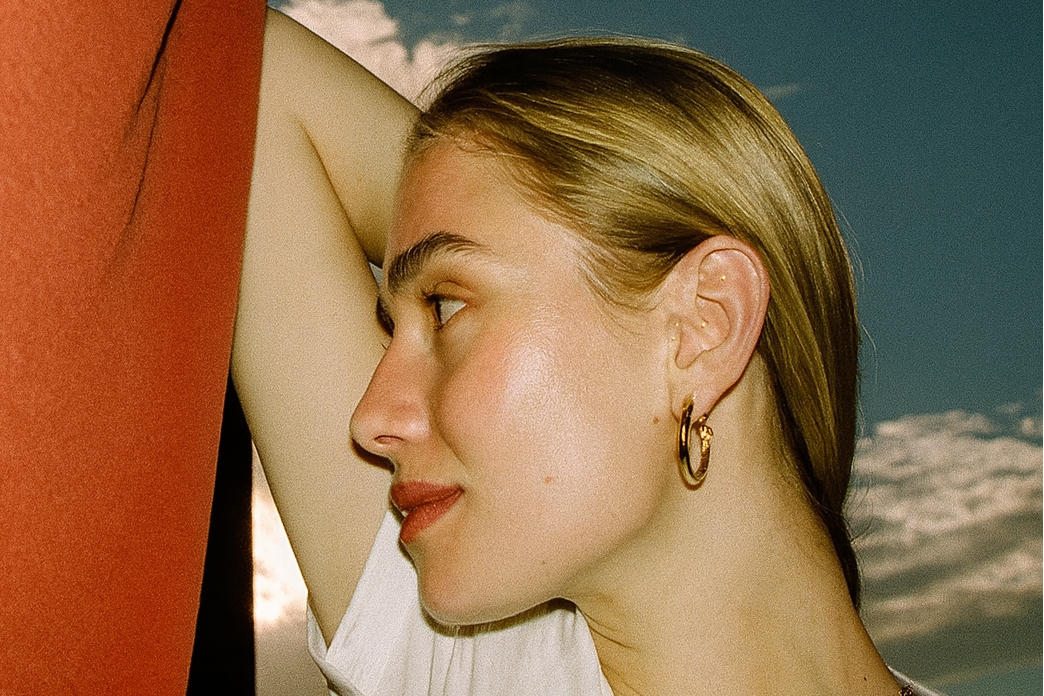 Woman with blonde hair, wearing earrings and ear seeds against a sky background