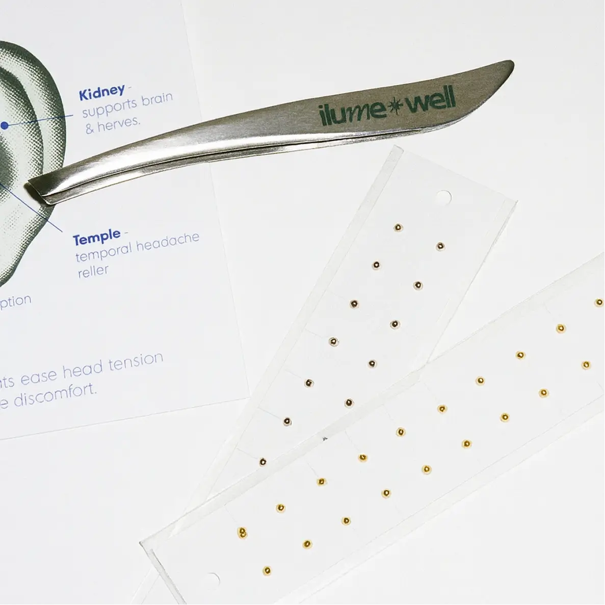 Tweezers with 'ilumewell' branding on a white background with gold acupressure ear seeds trips