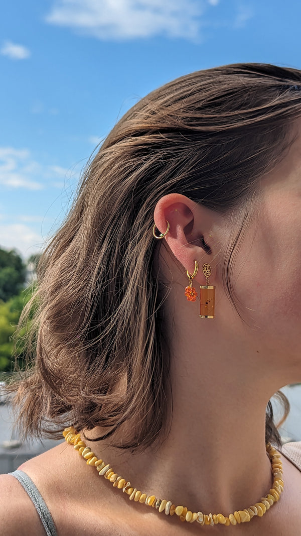 Close-up of a person wearing gold ear seeds with a scenic background
