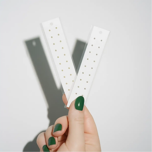 Hand holding two white ear seed strips with small round pellets against a light gray background