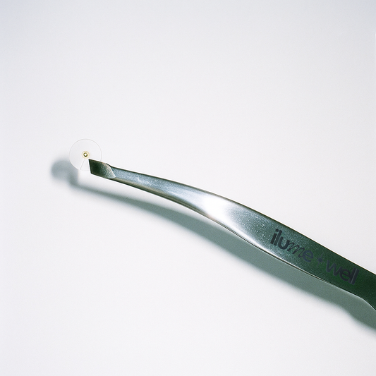 Metallic tweezer with 'ilumewell' branding, holding gold ear seeds on a white background
